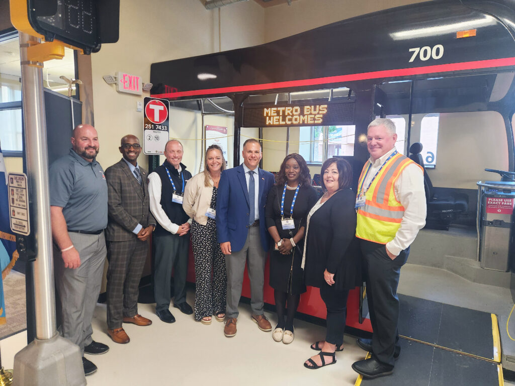 Metro Bus Marketing & Communications Manager, Nate Ramacher, Metro Bus CEO, Ryan I. Daniel, Metro Bus COO, Dave Green, Metro Bus CAO, Sunny Hesse, FTA Administrator Marc Molinaro, Metro Bus CFO Nene Israel, Metro Bus Community Outreach & Mobility Manager, Debbie Anderson and Metro Bus Training & Safety Manager Scott Stark standing in front of the training bus at the Metro Bus Mobility Training Center.