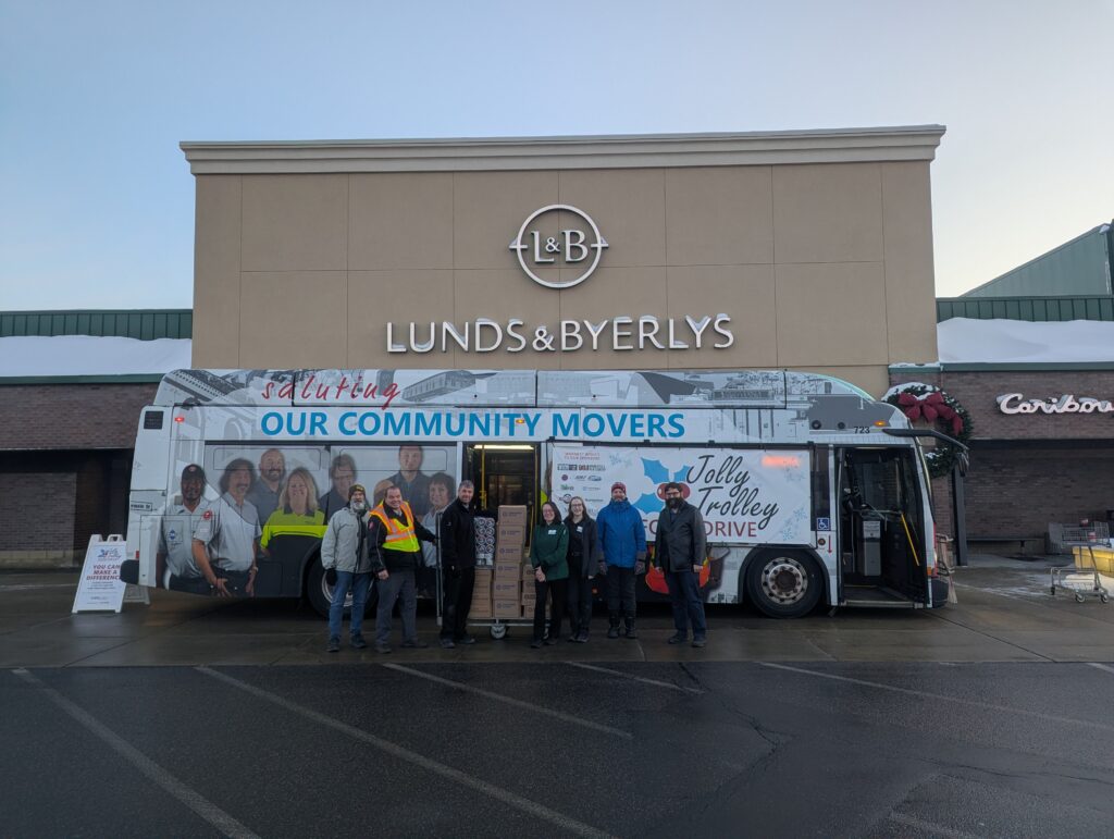 A group of people stand in front of a Metro Bus with a palette of boxed food.