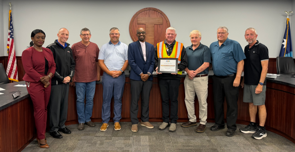 Metro Bus staff and board members standing in front of the dias in the Metro Bus Board Room. Training and Safety Manager Scott Stark is holding the Governor's Workplace Safety Award plaque.